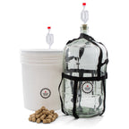 Master Vintner wine making fermenting setup with plastic bucket and glass carboy, both equipped with airlocks, plus a pile of wine corks in front.