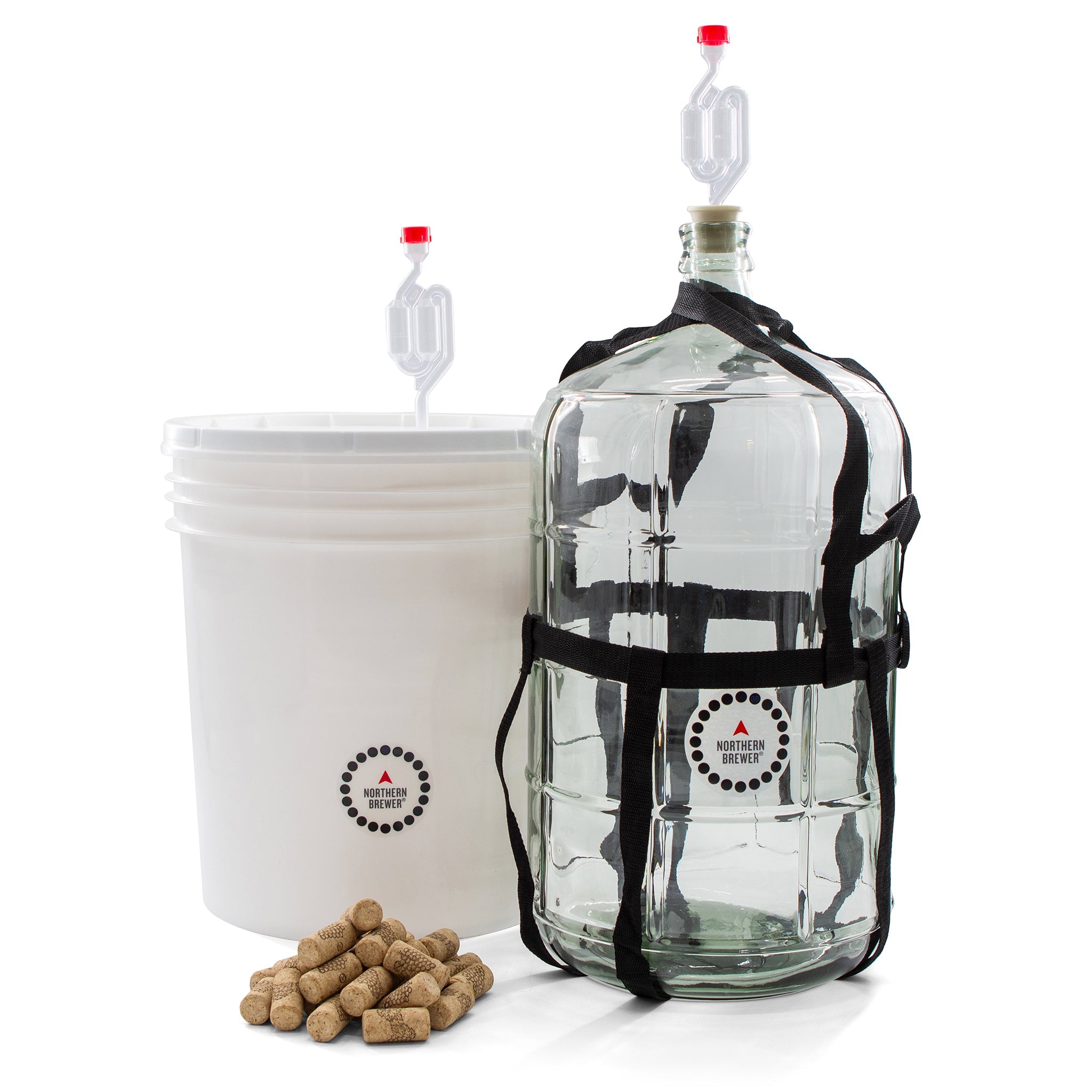 Master Vintner wine making fermenting setup with plastic bucket and glass carboy, both equipped with airlocks, plus a pile of wine corks in front.