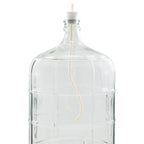 Clear glass carboy fitted with a drilled stopper and wine whip degassing tool, used to remove CO₂ from finished wine during the degassing stage of home wine making.