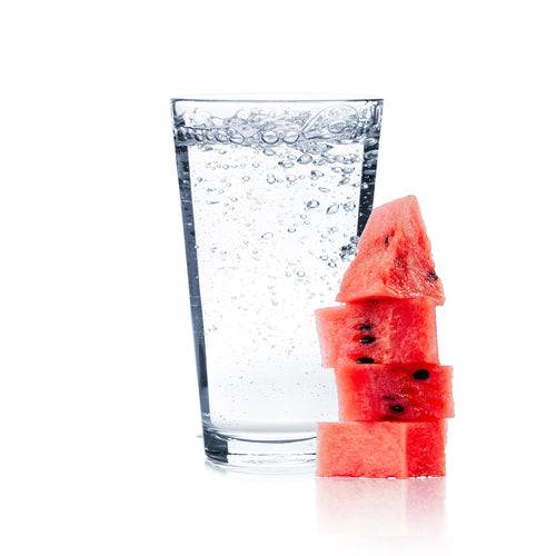A glass of Watermelon Hard Seltzer with watermelon slices next to it.