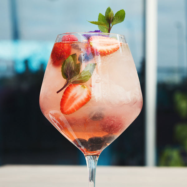 Pink cocktail with strawberries and mint leaves in a glass against a blurred outdoor background
