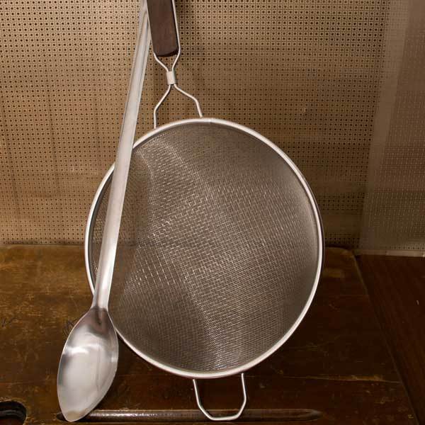 21-inch stainless steel spoon resting on top of a double-mesh stainless steel strainer