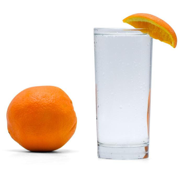 Navel Orange Hard Seltzer in a glass with an orange wedge and orange adjacent